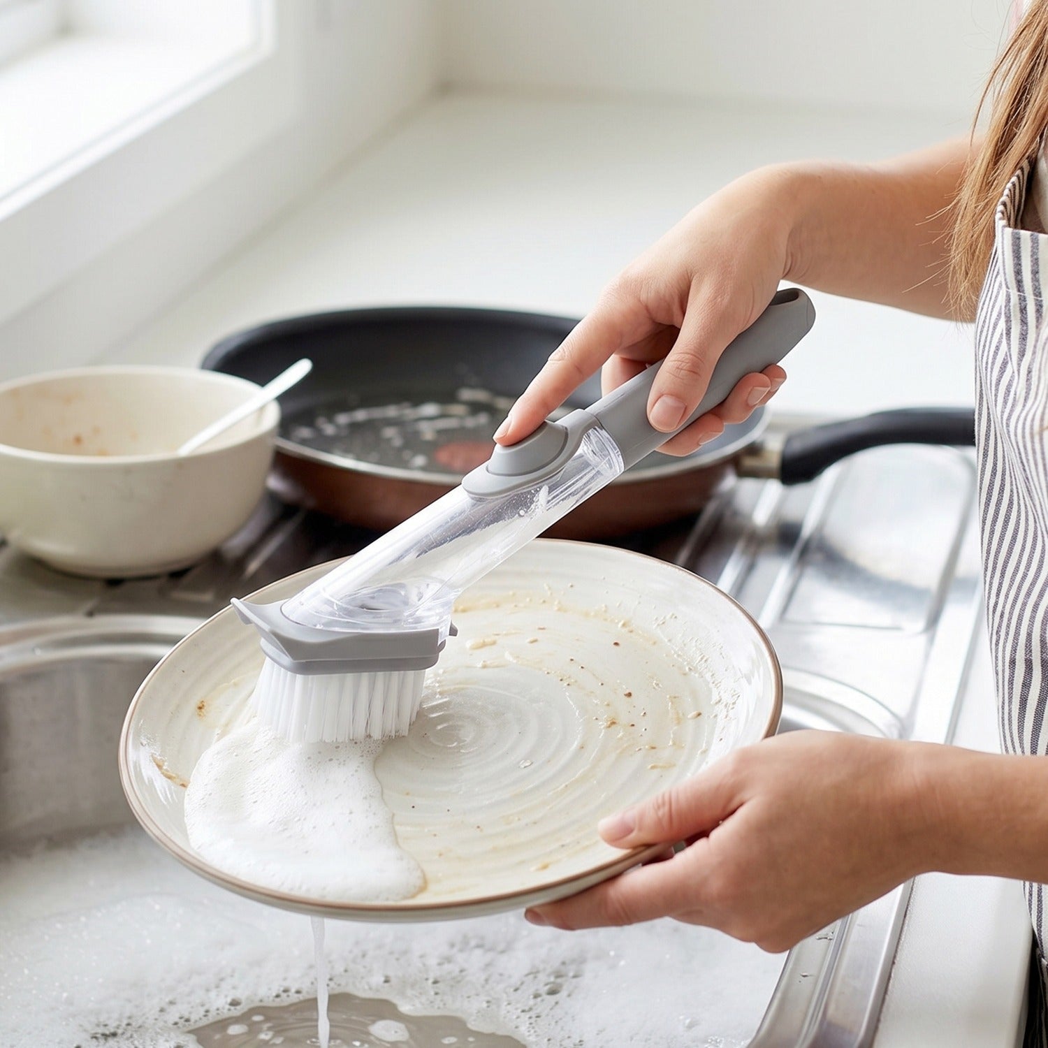 Hand holding soap dispensing dish scrub brush during cleaning